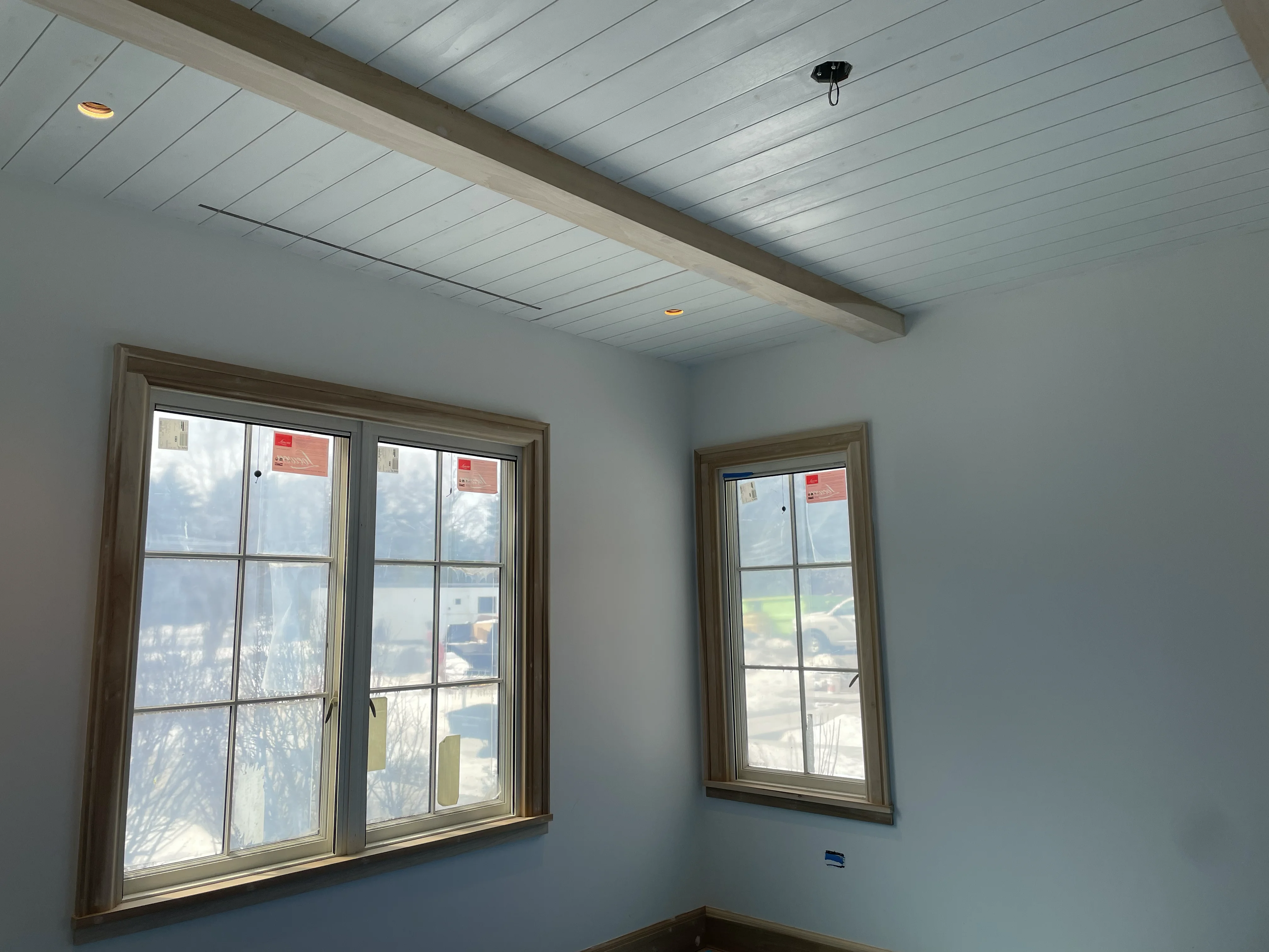 Shiplap ceiling with exposed beam and custom wood-trimmed windows by Gerhard and Sons
